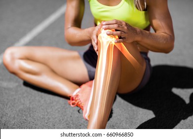 Low section of sportswoman suffering from knee pain while sitting on track during sunny day - Powered by Shutterstock