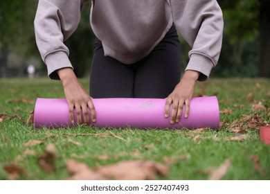 Low section of woman rolling up yoga mat on grass in park - Powered by Shutterstock