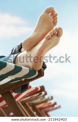 Low section of woman's feet relaxing on deckchair at beach