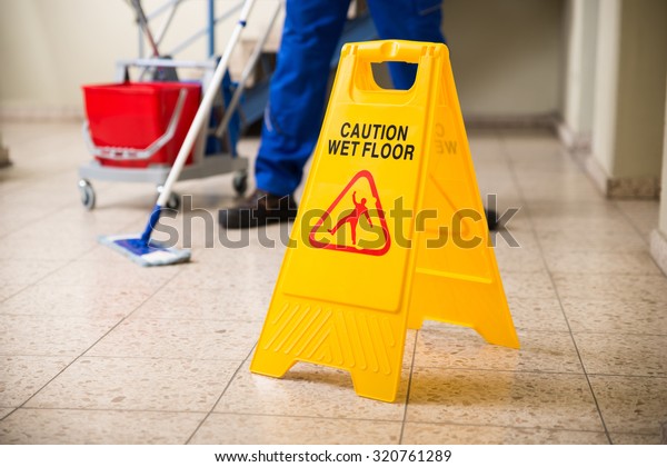 Low Section Of Worker Mopping Floor With Wet Floor\
Caution Sign On Floor