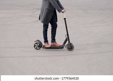 Low section of young contemporary businessman in coat, pants and boots standing on electric scooter while moving to work in the morning - Powered by Shutterstock