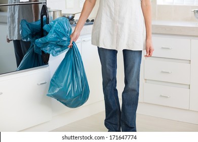 Low Section Of A Young Woman Carrying Garbage Bag In The Kitchen At House