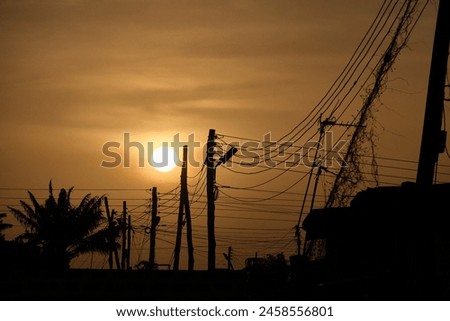 Low setting full round sun with electricity and telephone cable wires in silhouette, Accra, Ghana