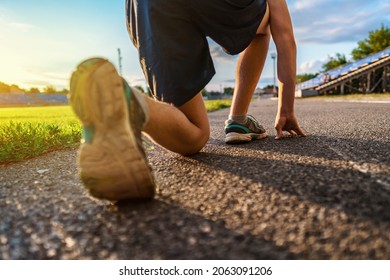 Low Start For Running, Close Leg View, Teen Boy Runs Along The Stadium Track, A Soccer Field With Green Grass - Concept Of Sports And Health