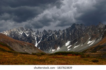 The Low Stormy Clouds Touch Top Of Snowy Mountain. Dismal Overcast Awesome Landscape With Big Rocks And Glacier