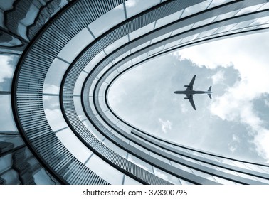 Low view blue colorized picture of modern architecture building with landing airplane in background  - Powered by Shutterstock