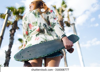 Low view of a hipster girl holding long board with copy space area for your brand while standing against sky and palm trees resting after riding, young woman with skateboard relaxing after skating - Powered by Shutterstock