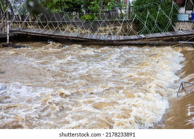 A low view of the river flowing violently past a broken wooden bridge near the bank of an old wooden fence inside a temple in rural Thailand.
