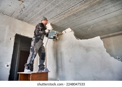 Low view of worker with demolition hammer who breaking interoom wall. General repair at home with crashing of wall separating two rooms for creating one large living room.