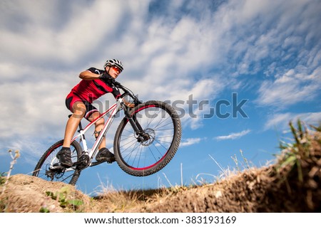 Low, wide angle portrait against blue sky of mountain biker going downhill. Cyclist in red sport equipment and helmet
