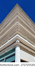 Low-angle architectural photograph capturing the sharp triangular corner of a modern multi-story building against a vivid blue sky, emphasizing geometric lines, minimalism, and contemporary design.
