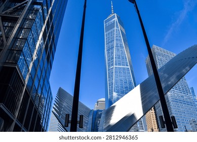 Low-angle architectural view of One World Trade Center framed by the sweeping white structure of the Oculus transportation hub in Lower Manhattan, New York City, against a vibrant blue sky.