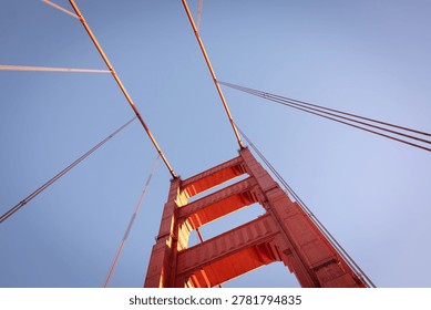A low-angle, architectural view of a tower on the Golden Gate Bridge in San Francisco. The bridge is famous for its distinctive reddish-orange color, officially known as International Orange. 