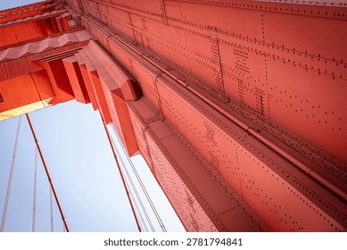 A low-angle, architectural view of a tower on the Golden Gate Bridge in San Francisco. The bridge is famous for its distinctive reddish-orange color, officially known as International Orange. 
