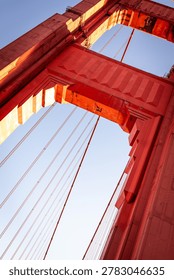 A low-angle, architectural view of a tower on the Golden Gate Bridge in San Francisco. The bridge is famous for its distinctive reddish-orange color, officially known as International Orange. 