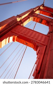 A low-angle, architectural view of a tower on the Golden Gate Bridge in San Francisco. The bridge is famous for its distinctive reddish-orange color, officially known as International Orange. 