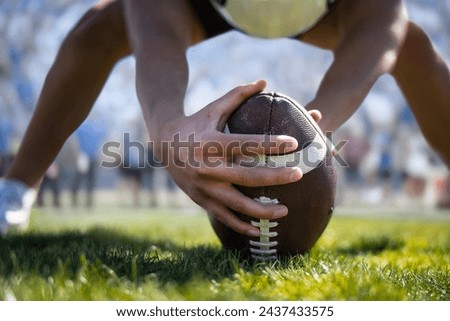 Low-angle close up view of a football player hiking a football during a football game. Focus on the ball and hands. Selective focus image. Unique view.	
