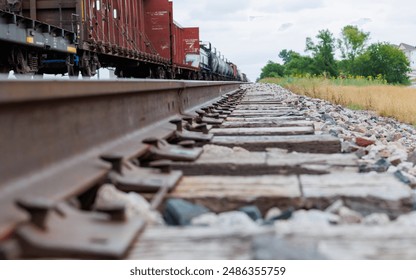 Low-angle close-up of railway tracks with a freight train moving in the background. focus on the metal rails and wooden sleepers