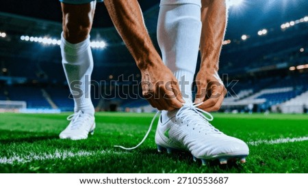 A low-angle, close-up view captures the intense moment a soccer player adjusts the white laces on his cleat, preparing for intense competition on the vibrant green pitch.
