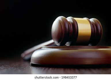 Low-angle close-up of a vintage classical gavel placed on a round sound block, on a wooden table, with copy space on black background