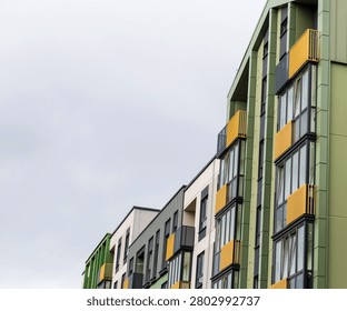 Low-angle diagonal view of a modern multi-colored apartment building row featuring green facades and bright yellow geometric balconies.