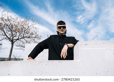 A low-angle front view of a young white man from Generation Z looking at the camera in an outdoor park