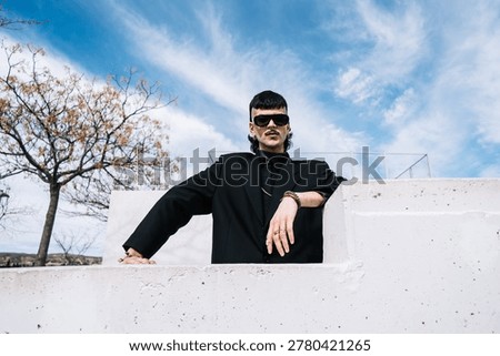 A low-angle front view of a young white man from Generation Z looking at the camera in an outdoor park