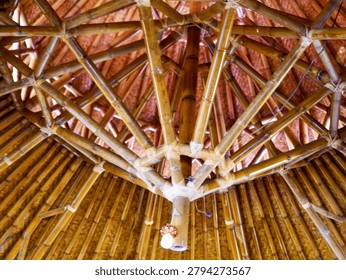 A low-angle interior view of a complex dome-shaped bamboo roof structure with intricate radial framing and tightly wrapped rattan joints.