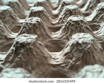 A low-angle macro shot capturing the rhythmic valley and peak structure of a brown recycled paper pulp egg container. The camera angle emphasizes the mountain-and-valley landscape formed by the molded paper cups, with soft lighting creating contrasting highlights and subtle deep shadows along the structural grooves. The foreground pulp ridges are crisp and clear, showing individual raw fibers, while the background elements softly recede into focus-blur depth. This striking graphic visual is excellent for eco-conscious product banners, circular economy educational materials, agricultural supply packaging catalogs, sustainable design headers, and industrial texture collections seeking an artistic, architectural perspective on simple biodegradable paper pulp materials.
