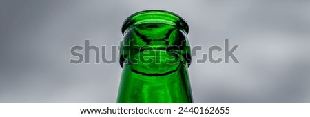 Low-angle perspective captures the bottleneck of an empty green beer bottle against a backdrop of overcast sky, offering a visual contrast and potential for versatile use in various creative projects.