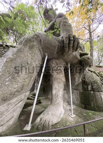 Low-angle perspective capturing stone sculpture depicting mythical battle between ogre and Proteus, emphasizing dramatic sculptural narrative within Parco dei Mostri landscape