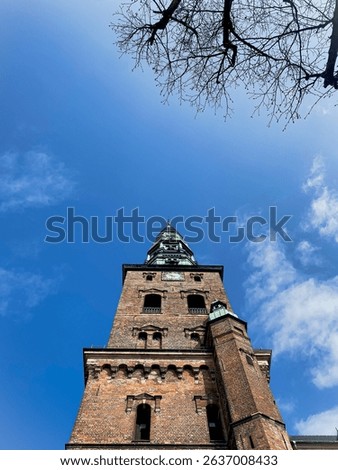 A low-angle perspective highlights the weathered red brick texture and green copper details of the Nikolaj Kunsthal church tower, evoking a grand and timeless architectural presence.