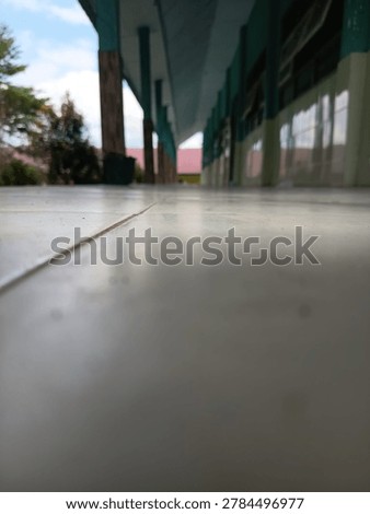 Low-angle perspective of an outdoor school corridor tile floor with blurred pillars and roof structure