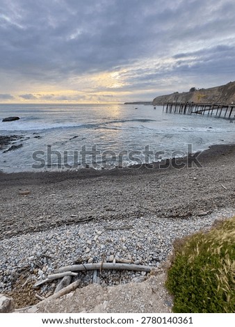 A low-angle perspective of smooth pebbles on the shoreline with the Point Arena pier and wharf in the distant background.