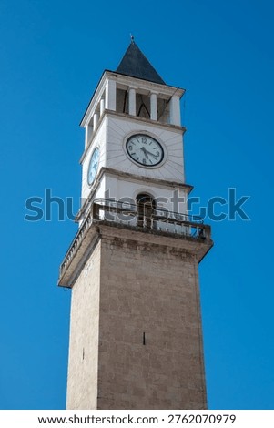 A low-angle perspective of Tirana's iconic white stone Clock Tower, showcasing its traditional architecture and prominent clock face under a bright blue sky in Tirana, Albania.