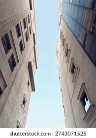 Low-angle perspective view between two tall buildings forming a geometric urban composition against a clear sky.
