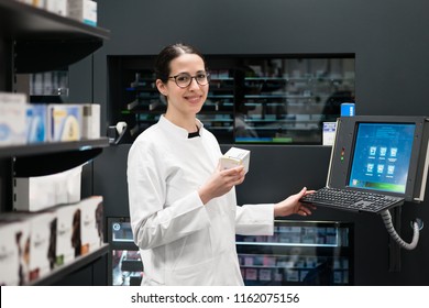 Low-angle Rear View Of An Experienced Female Pharmacist Using A Computer While Managing The Drug Stock In A Contemporary Pharmacy With Modern Technology