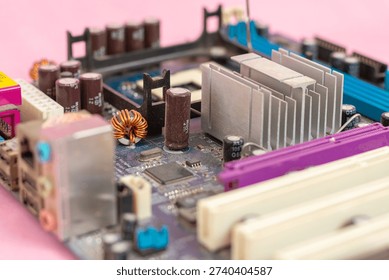 Low-angle, selective focus view of a computer motherboard featuring a silver aluminum heatsink, capacitors, and electronic circuitry on a pink background. Concept of hardware cooling
