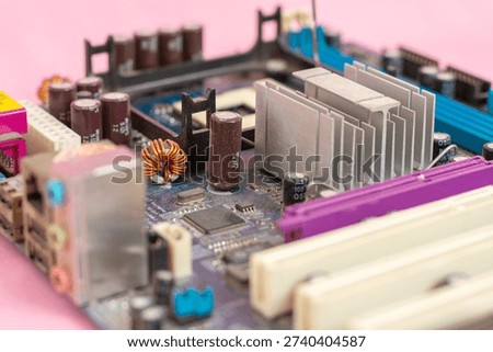 Low-angle, selective focus view of a computer motherboard featuring a silver aluminum heatsink, capacitors, and electronic circuitry on a pink background. Concept of hardware cooling