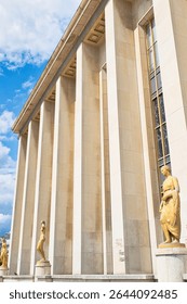 Low-angle shot of a building with columns and statues, graffiti on lower portion.  Blue sky with clouds visible in upper left corner.