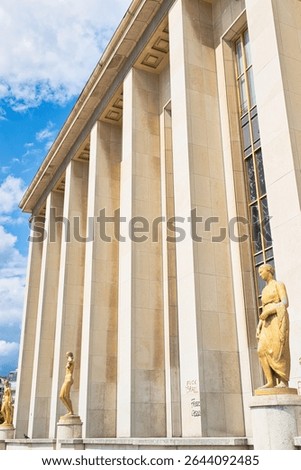Low-angle shot of a building with columns and statues, graffiti on lower portion.  Blue sky with clouds visible in upper left corner.