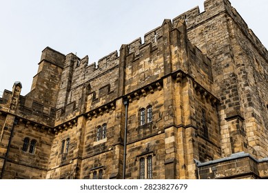 A low-angle shot captures the formidable stone walls of Lancaster Castle, highlighting its rugged, ancient architecture and crenellated battlements against a bright sky - Lancaster Castle, Lancaster, UK