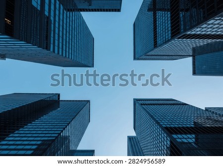 A low-angle shot captures the imposing architecture of contemporary skyscrapers reaching towards a vast, cloudless blue sky, emphasizing their scale and design.