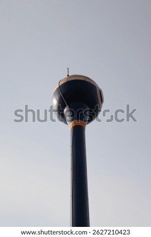 Low-angle shot capturing the underside of a water storage tank set in a rural agricultural field, highlighting infrastructure and farming environment.