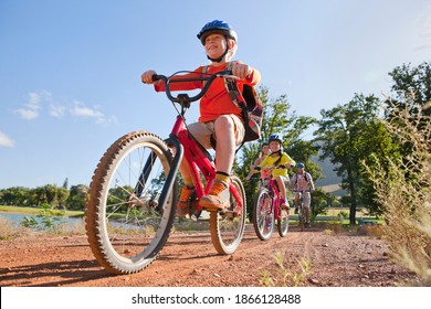 Low-angle Shot Of A Couple Mountain Biking With Their Children Along A Pathway By The Lake At The Countryside.