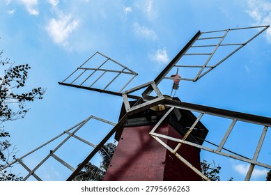 A low-angle shot of a decorative windmill with a red base and metal blades against a bright blue sky.