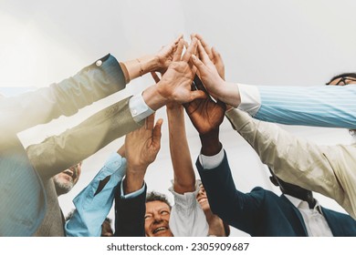 Low-angle shot of a diverse team of colleagues in a bright office. They are standing together, giving a group high five. The focus is on the hands, with light flares entering the lens