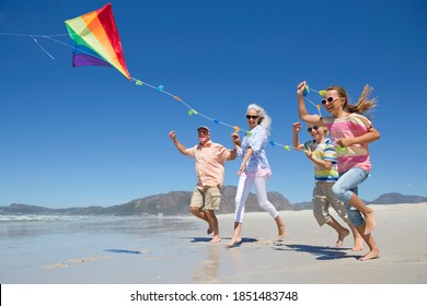 Low-angle shot of an elderly couple chasing a kite with their grandchildren on a sunny beach. - Powered by Shutterstock