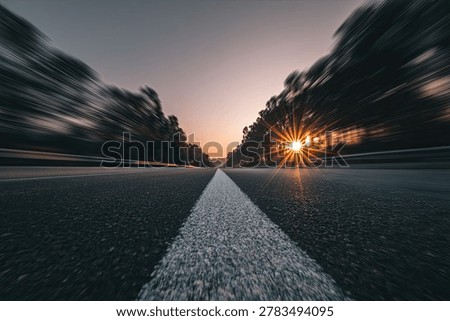 A low-angle shot of an empty highway stretching towards a vibrant sunset, with trees on either side blurred by motion.