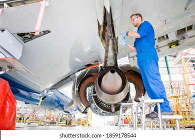 Low-angle shot of an engineer working under the wing of a passenger jet at a hangar.